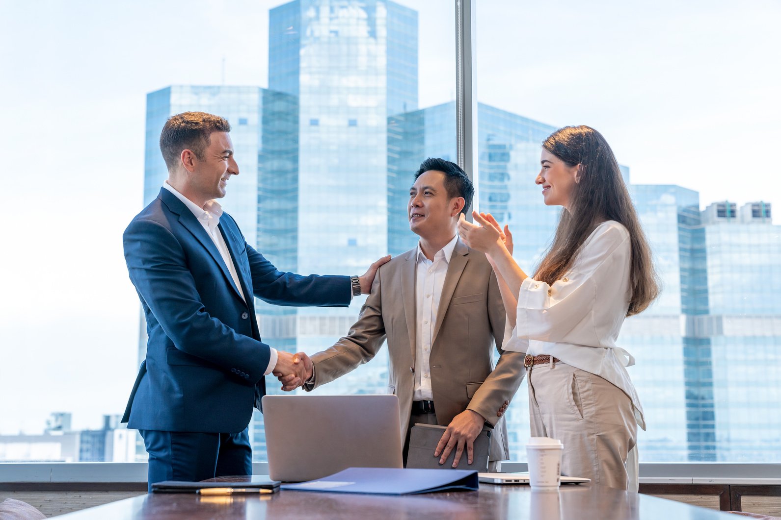 Caucasian boss handshake Asian employee congratulating with work success